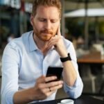 homem preocupado olhando o celular com notificacao de nome negativado indevidamente