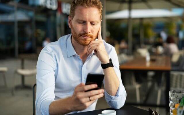 homem preocupado olhando o celular com notificacao de nome negativado indevidamente